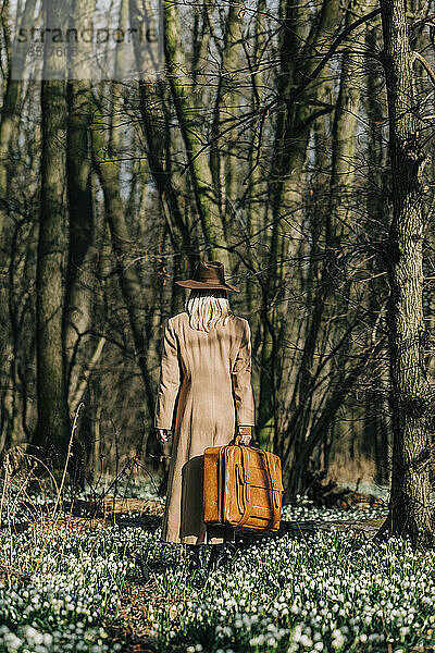 Frau mit Koffer geht im Wald spazieren