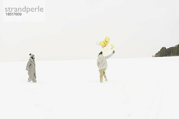 Frau hält Luftballons und hat Spaß mit Freund im Schnee