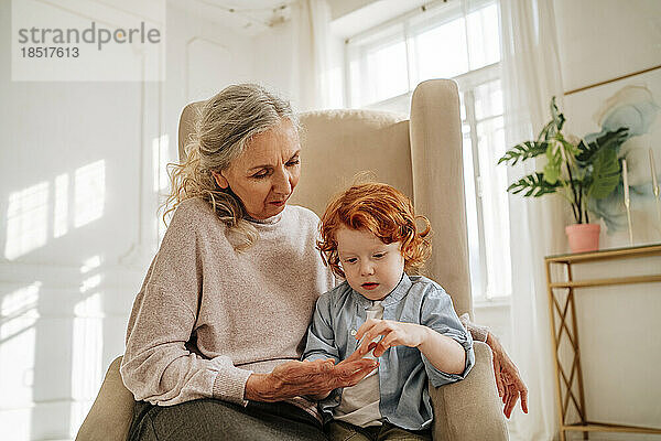 Junge berührt Hand seiner Großmutter  die zu Hause auf einem Sessel sitzt