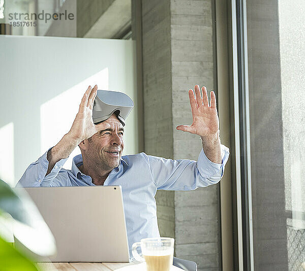 Glücklicher Geschäftsmann mit VR-Brille gestikuliert im Büro