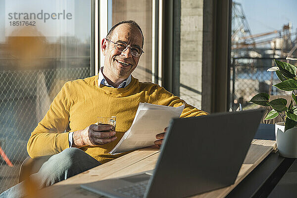 Glücklicher Geschäftsmann mit Dokument beim Kaffee im Büro