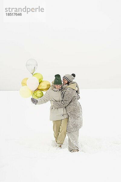 Freunde in warmer Kleidung mit gelben Luftballons genießen den Schnee