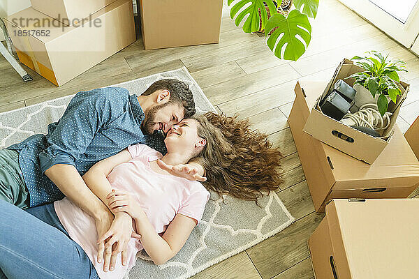 Liebevolles Paar liegt im neuen Zuhause auf dem Teppich neben Kartons
