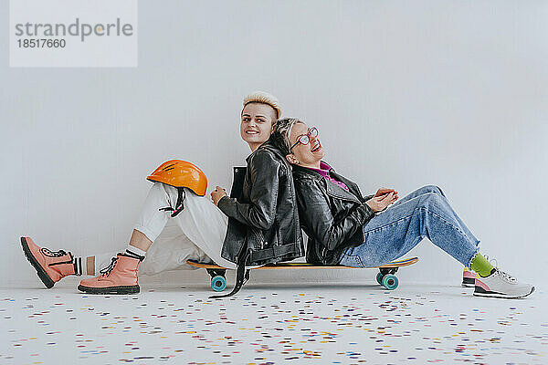 Mutter und Tochter sitzen Rücken an Rücken auf dem Skateboard