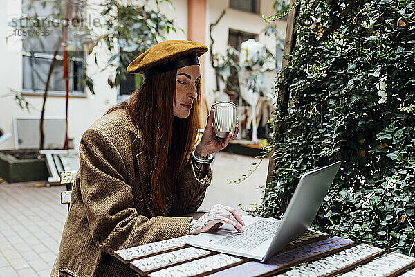 Frau mit Kaffeetasse und Laptop im Straßencafé