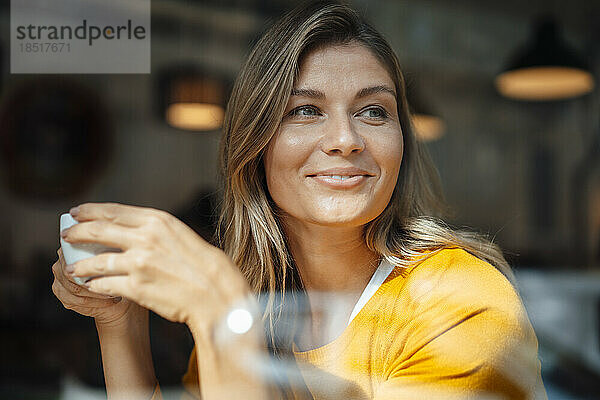 Lächelnde Frau mit Kaffeetasse im Café durch Glas gesehen