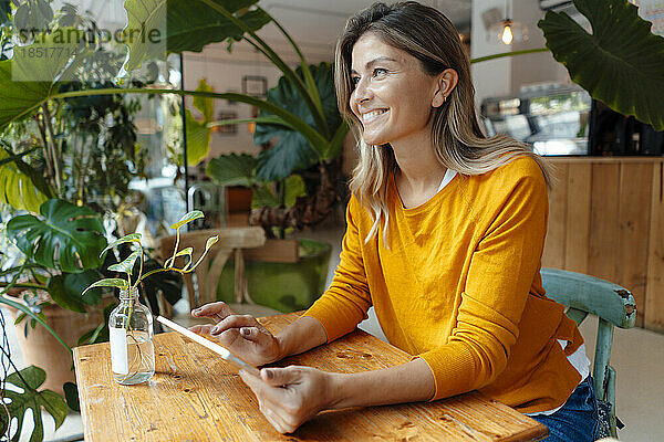 Happy woman with tablet PC sitting by plants in cafe