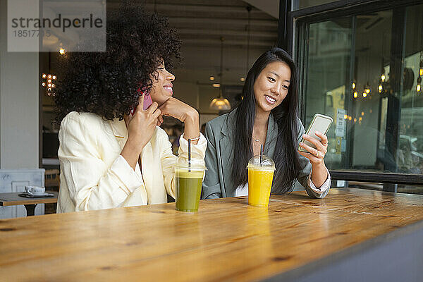 Freunde nutzen Smartphones und sitzen mit Saft am Tisch im Café