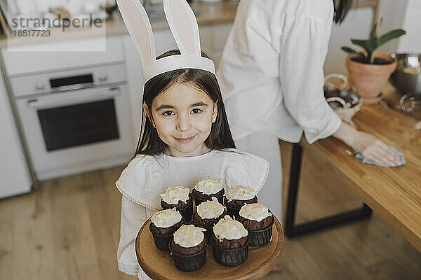 Lächelndes Mädchen hält Cupcakes am Ostertag zu Hause