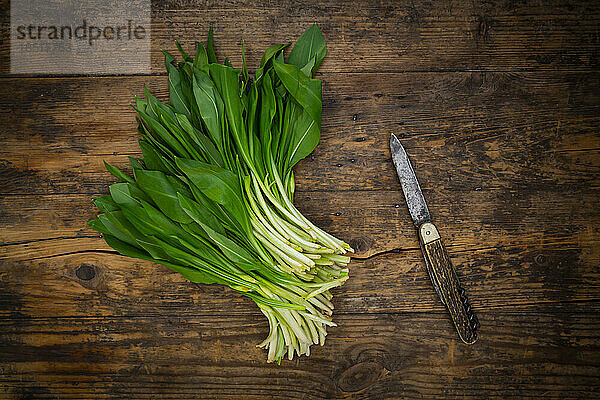 Fresh ramson and kitchen knife lying on wooden surface