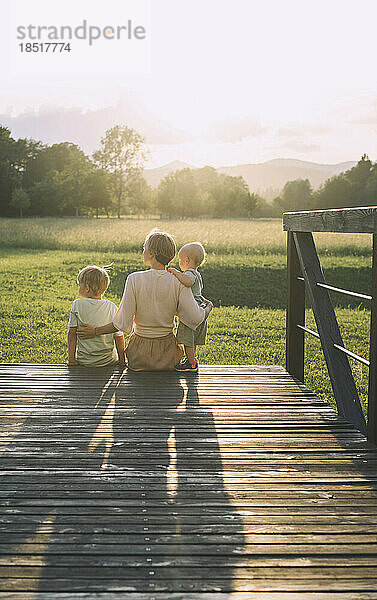 Mother sitting with sons on wooden footbridge