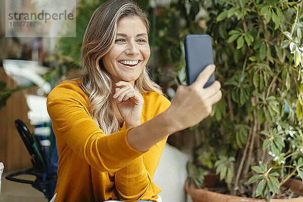 Glückliche Frau  die im Café ein Selfie mit der Pflanze macht