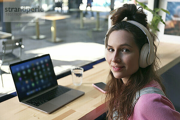 Junger Freiberufler trägt kabellose Kopfhörer im Café