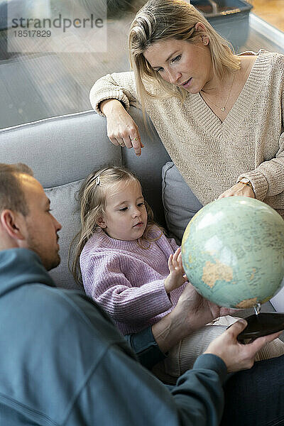 Tochter und Eltern sitzen mit Globus zu Hause auf dem Sofa