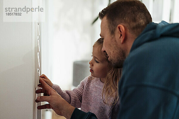 Mädchen und Vater regeln zu Hause die Temperatur am Thermostat