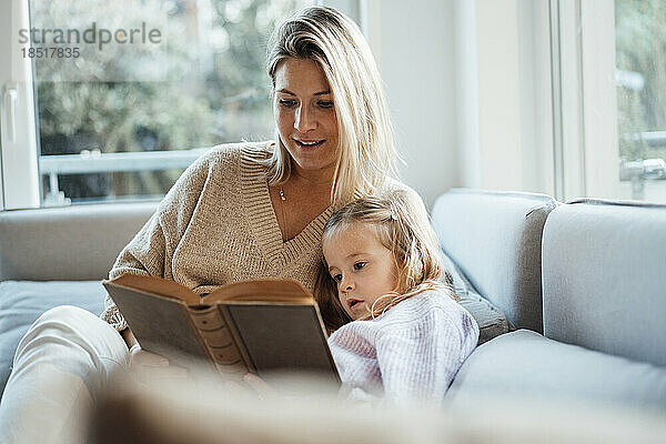 Mother reading book to daughter at home
