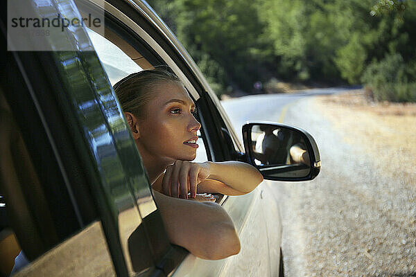 Nachdenkliche junge Frau lehnt am Autofenster