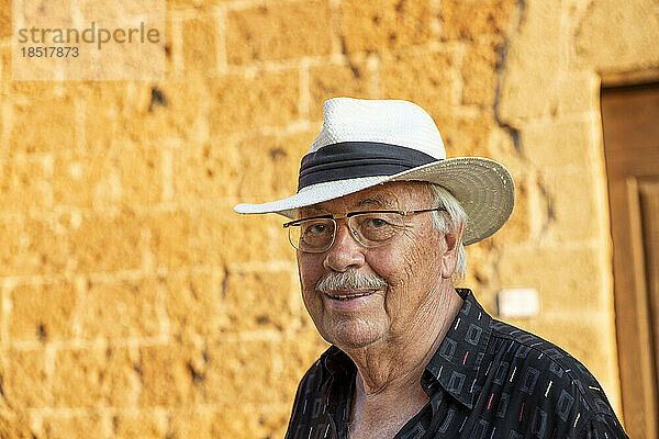 Lächelnder älterer Mann mit Hut vor der Wand