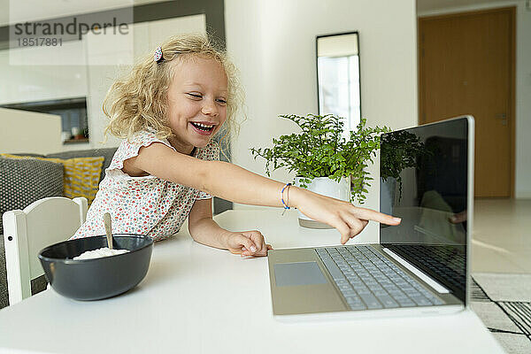 Happy girl pointing at laptop screen on table at home
