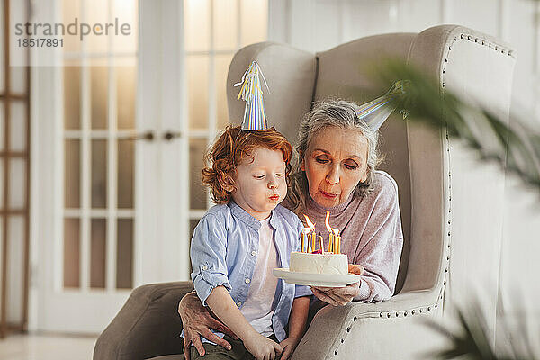 Junge mit Großmutter bläst zu Hause Kerzen auf Geburtstagstorte