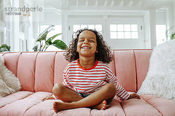 Glückliches Mädchen  das zu Hause auf einem rosa Sofa im Wohnzimmer sitzt