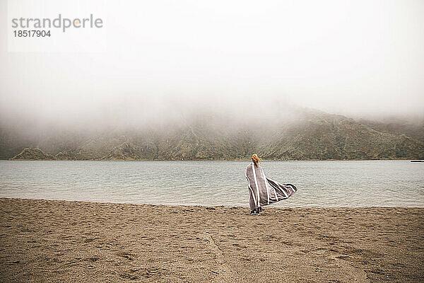 Frau im Poncho steht vor dem See