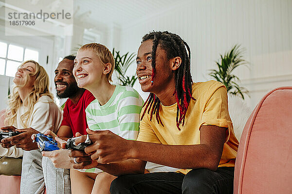 Lächelnder junger Mann mit Dreadlocks  der zu Hause mit Freunden ein Videospiel spielt