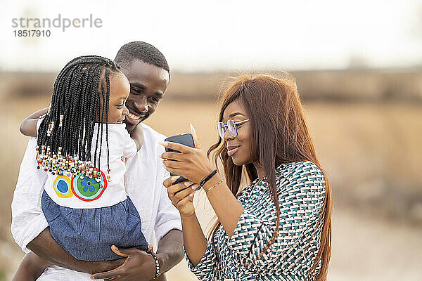 Lächelnde Frau zeigt Mann und Tochter ihr Smartphone