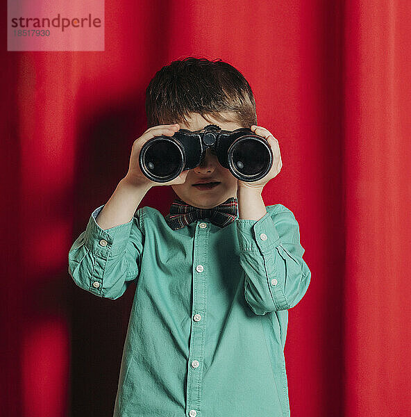 Boy looking through binoculars in front of curtain