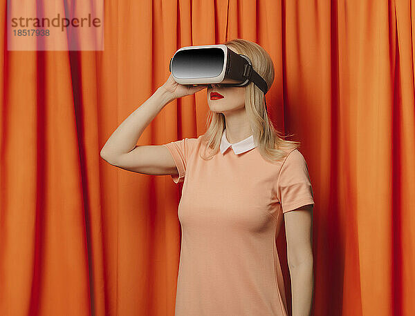 Frau mit Virtual-Reality-Simulator steht vor orangefarbenen Vorhängen