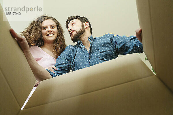 Glückliches junges Paar öffnet Karton im neuen Zuhause