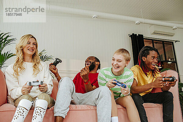 Aufgeregter junger Mann spielt Videospiel mit Freunden auf dem Sofa