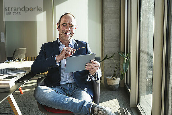 Glücklicher reifer Geschäftsmann mit Tablet-PC  der im Büro sitzt