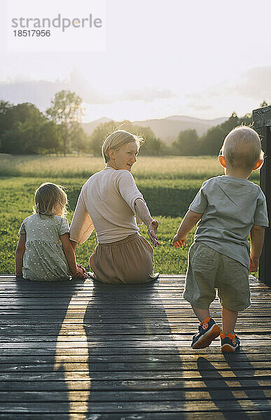 Mutter sitzt mit Tochter und Sohn auf einem Holzsteg