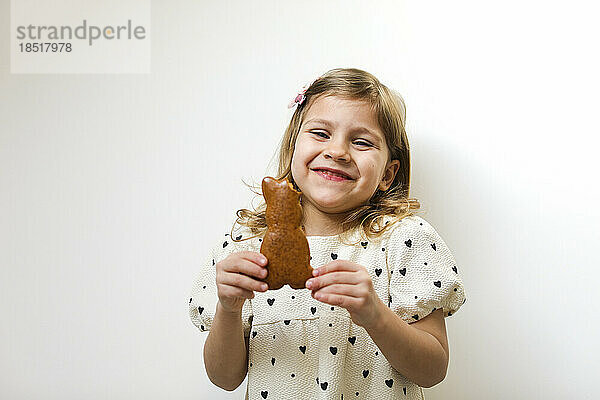 Glückliches Mädchen hält Hasenform-Lebkuchen vor weißem Hintergrund