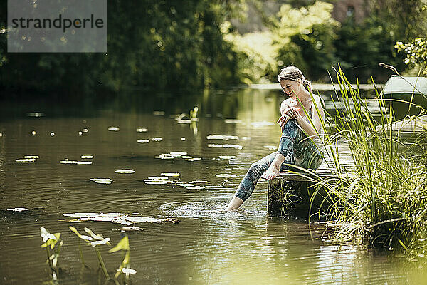 Frau taucht ihr Bein ins Wasser und sitzt am See
