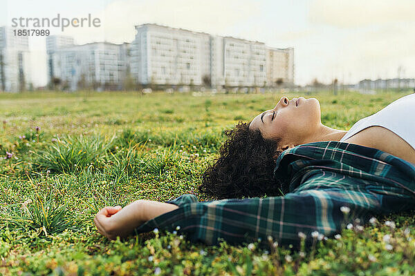 Junge Frau mit geschlossenen Augen entspannt sich bei Sonnenuntergang im Gras