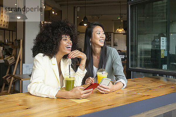 Glückliche Freunde mit Smartphone sitzen im Café