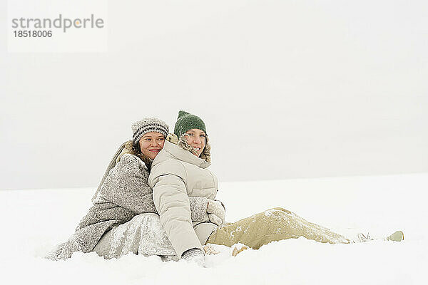 Frau umarmt Freundin von hinten im Schnee sitzend