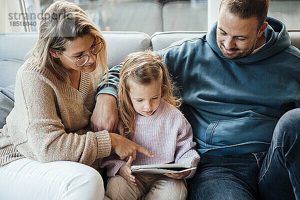 Tochter sitzt mit ihren Eltern auf dem Sofa im Wohnzimmer und benutzt einen Tablet-PC