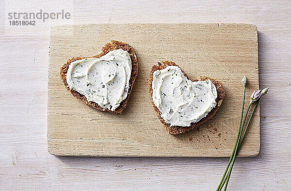 Two heart shaped sandwiches with cream cheese and chives on cutting board