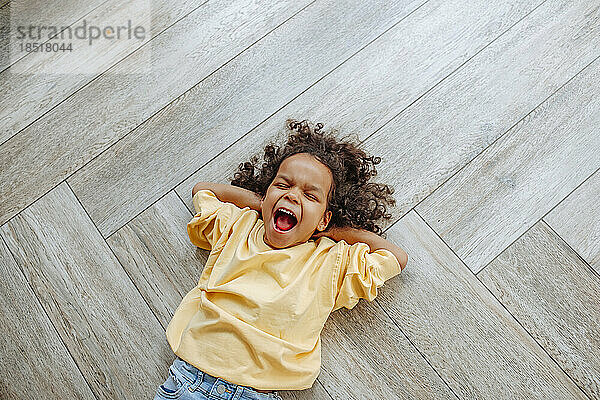 Cute girl yawning and lying on wooden floor at home