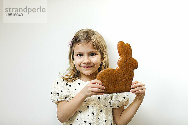 Lächelndes Mädchen hält Lebkuchen-Osterhasen vor weißem Hintergrund