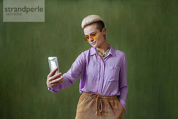 Junge Frau mit Sonnenbrille macht ein Selfie vor einer grünen Wand