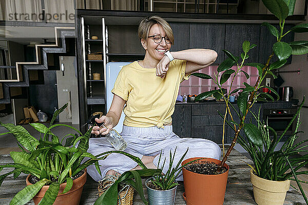 Glückliche Frau  die zu Hause eine Smartwatch benutzt und Pflanzen gießt
