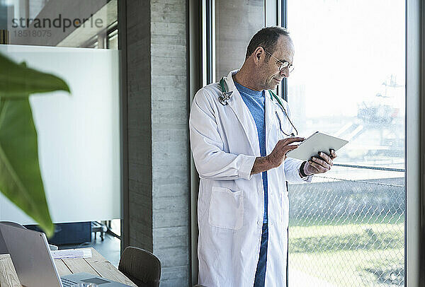 Arzt benutzt Tablet-Computer  der am Fenster steht