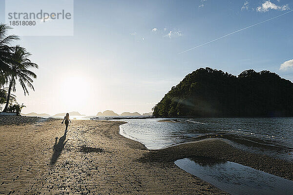 Junge Frau spaziert bei Sonnenuntergang am Strand