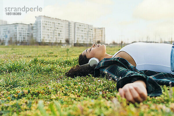 Junge Frau mit geschlossenen Augen entspannt sich und hört Musik im Gras bei Sonnenuntergang