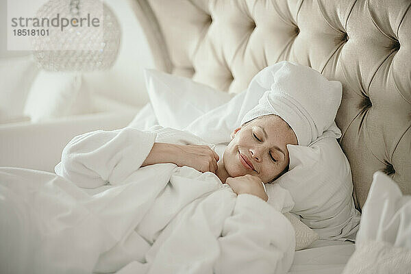 Lächelnde Frau entspannt sich mit geschlossenen Augen zu Hause im Bett
