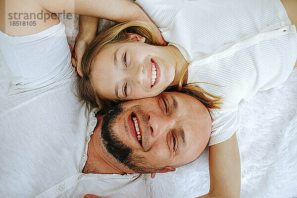 Happy father and daughter lying on bed at home